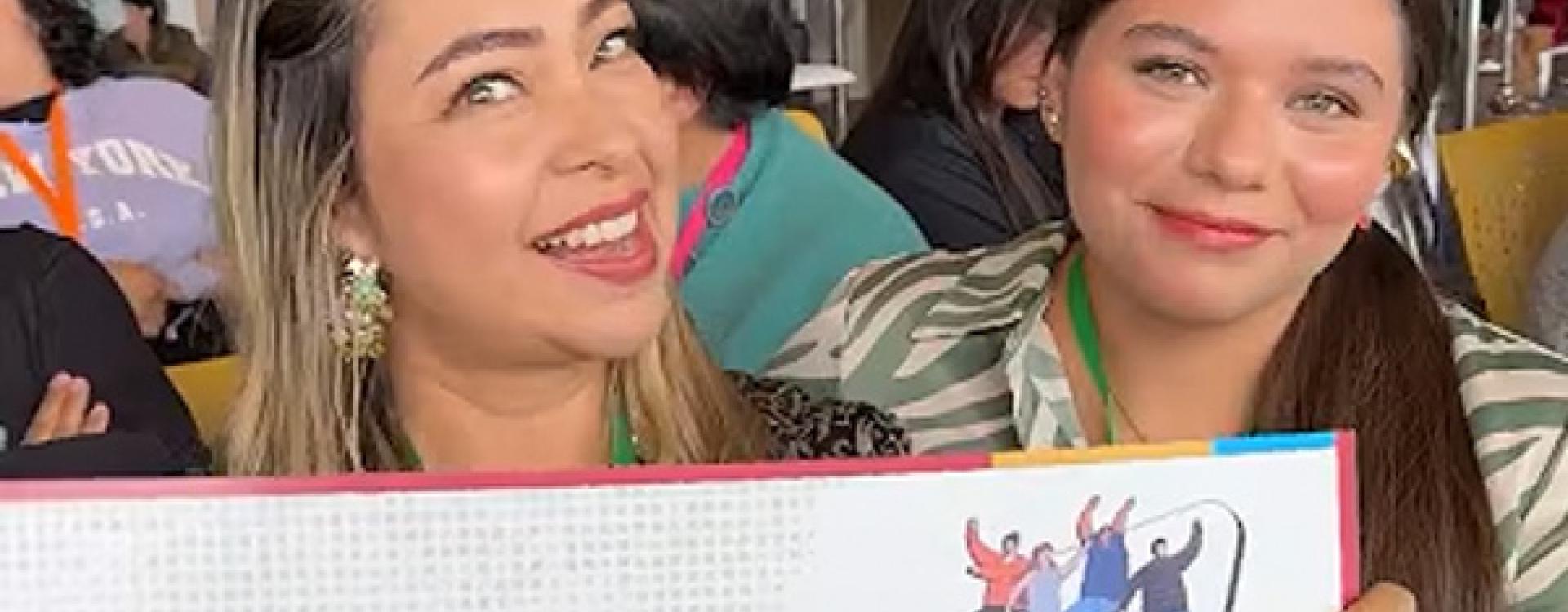 Mujeres sonriendo a la cámara con diplomas de premiación.