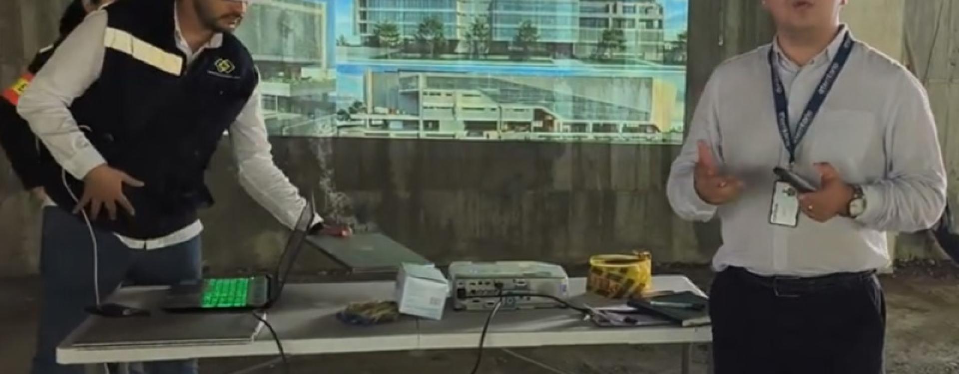 Persona con casco exponiendo un render de un edificio dentro de la obra en gris.